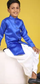 Kid in blue traditional attire against yellow backdrop.