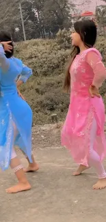 Two women in vibrant traditional dresses dancing outdoors.