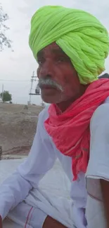 Elderly man in neon green turban and pink scarf with a serene desert backdrop.