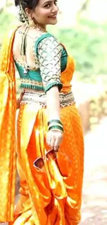 Woman in vibrant orange saree with green blouse, smiling outdoors.