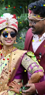 Joyful couple in traditional attire surrounded by greenery.