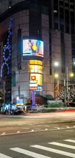 Night view of a city intersection with bright lights and tall buildings.