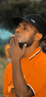 Man in orange shirt smoking with blurred outdoor background.