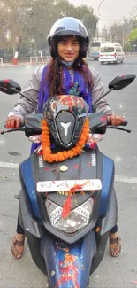 Woman riding a decorated blue scooter on city street.