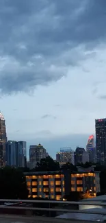 Skyline at dusk with lit skyscrapers under cloudy sky.