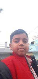 Boy in red jacket on urban street with buildings in background.