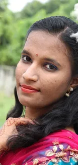 Woman in traditional attire against lush green background.