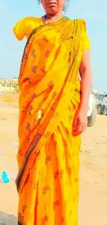 Woman in vibrant yellow saree on sandy background.