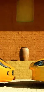 Two yellow sports cars by a rustic wall.