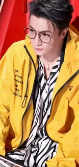 Man in a yellow jacket with glasses and striped shirt on a red chair.