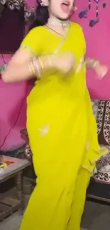 Woman dancing in yellow saree indoors.