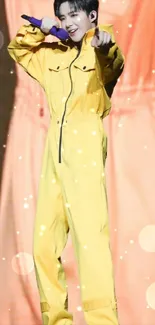 Performer in a yellow jumpsuit pointing with a smile on stage.