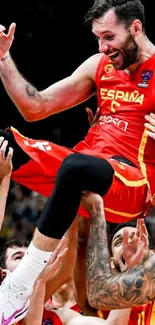 Basketball players celebrate lifting a teammate in vibrant red uniforms.