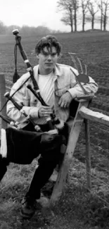 Vintage black and white photo of a bagpiper leaning on a fence in a field.