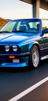 Vintage blue car driving on highway with scenic surroundings.