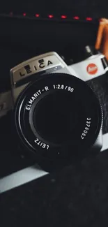 Vintage camera with black lens and leather strap on dark background.