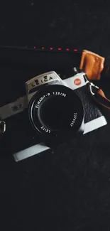 Vintage Leica camera with leather strap on a black surface.