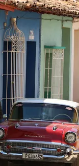 A vintage red car by colorful walls.