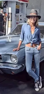 A woman in denim outfit stands by a vintage car at a gas station.