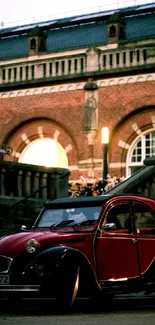 Vintage red car parked by a historic brick building in an urban setting.