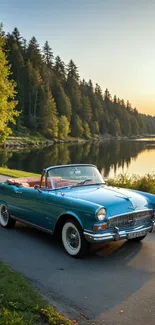 A blue vintage convertible by a lake with a forested backdrop at sunset.