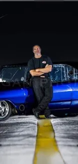 Man poses by blue vintage car on a night street.