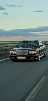 Classic car cruising on open highway under cloudy sky.