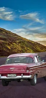 Vintage car on winding mountain road under a vibrant blue sky.