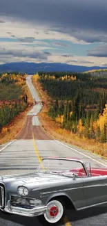 Vintage car on scenic road with autumn trees under a cloudy sky.