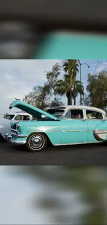 Vintage turquoise car at a show with trees and sky in the background.