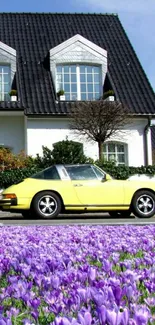 Vintage yellow car with purple flowers next to a white house.