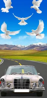 Vintage car with doves soaring in a blue sky over a mountain road.