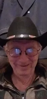 Smiling person wearing a cowboy hat and glasses with a rustic background.