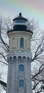 Vintage stone lighthouse with bare winter trees.