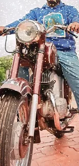 Vintage maroon motorcycle on a brick road with rider.