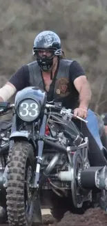 Man riding a vintage motorcycle on rough terrain, wearing a black helmet.