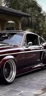 Vintage maroon muscle car parked on driveway with palm trees.