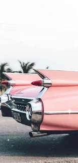 Vintage pink car with fins against a palm tree backdrop.