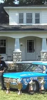 Vintage blue racing car with trophies in front of an old house.