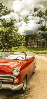 Vintage red convertible on a scenic, leafy road under a cloudy sky.