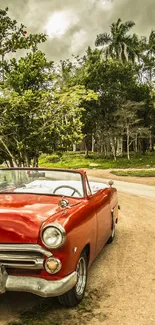 Vintage red car on rural road with lush trees and cloudy sky.