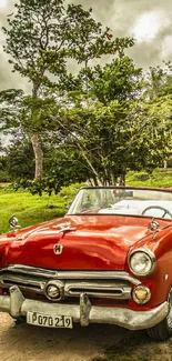 Red vintage convertible on a scenic rural road with lush green surroundings.