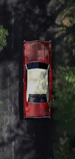 A vintage red car driving on a scenic forest road from an aerial view.
