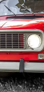 Close-up of a classic red car's headlight and grill.