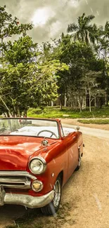 Vintage red convertible car on a rural road under dramatic skies.
