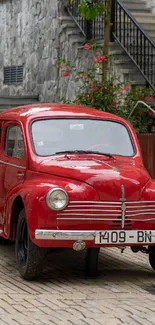 A vintage red car parked on a cobblestone street with stairs and flowers.