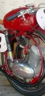 Vintage red motorcycle with race number two, parked by a beige wall.