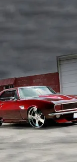 Vintage red muscle car parked outside a garage with chrome wheels.