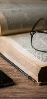 Open book with smartphone and glasses on wooden table background.