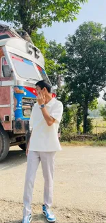 Person in casual attire standing by a vintage truck with trees.